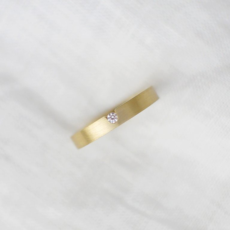 aliança de casamento feita à mão em ouro 18k e diamante central minimalista sobre fundo branco