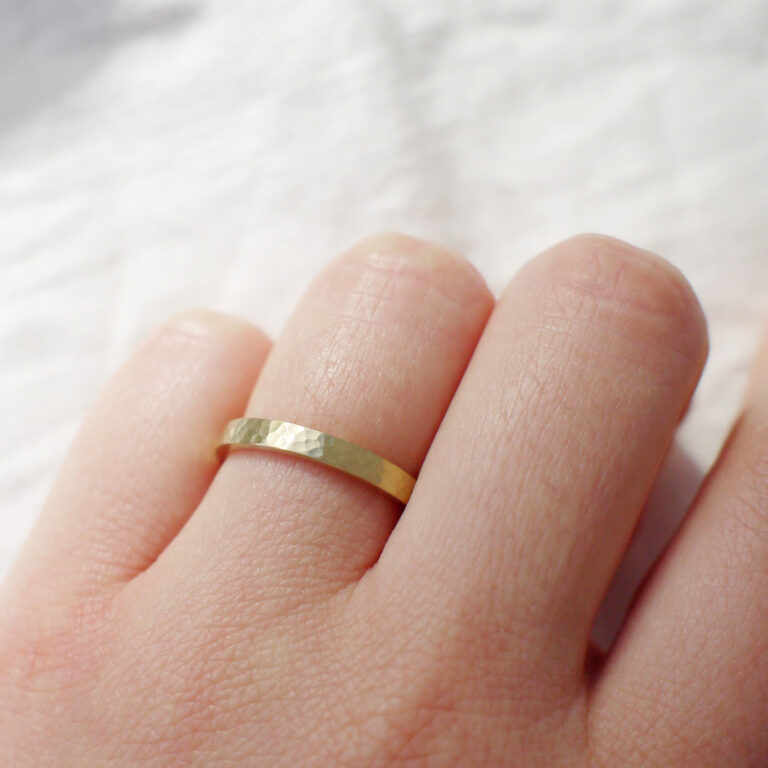 Mão feminina usando Aliança minimalista de 2,5mm de textura martelada feita a mão em ouro 18k