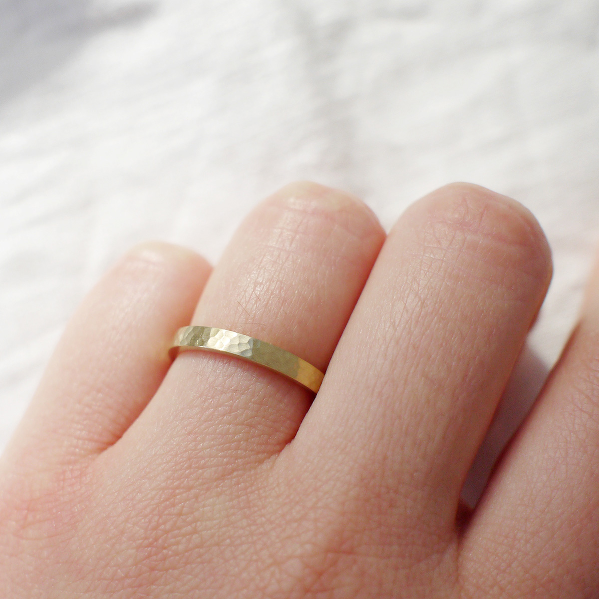 Mão feminina usando Aliança minimalista de 2,5mm de textura martelada feita a mão em ouro 18k