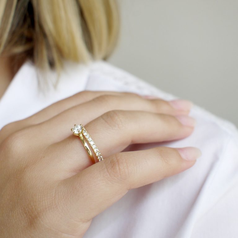 mulher usando aliança para casamentos feita à mão em ouro 18k com metade do aro cravejado de diamantes e anel de noivado com diamante