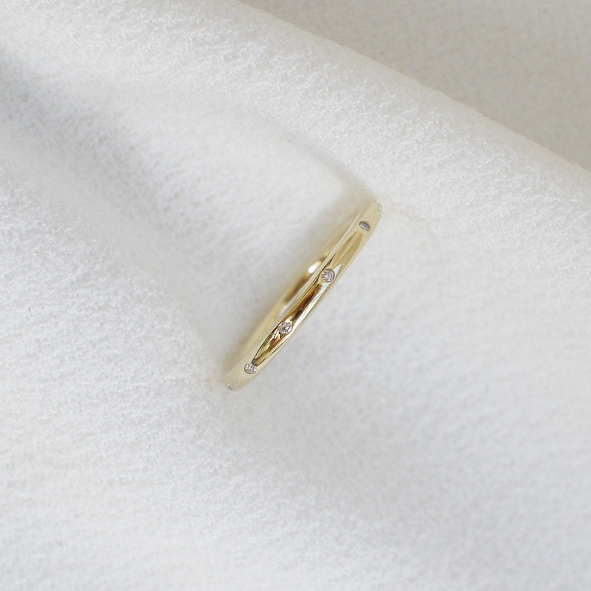 Aliança de aro redondo 1,8mm com diamantes minimalista feita a mão em ouro 18k para casamentos sobre tecido branco