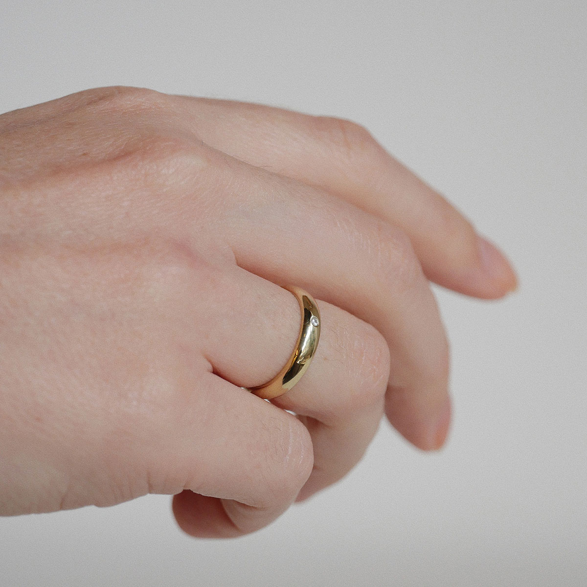 Mão feminina usando aliança de 4mm minimalista feita a mão em ouro 18k com diamantes para casamentos
