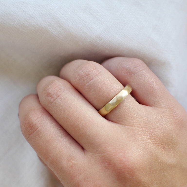 Mão feminina usando Aliança de casamento feita a mão em ouro 18k facetada minimalista sobre tecido branco