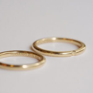 par alianças de casamento feita à mão em ouro 18k que o par forma um coração minimalista com gravação dos nomes do casal e data de casamento sobre fundo branco