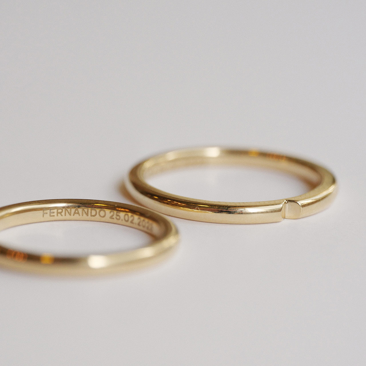 par alianças de casamento feita à mão em ouro 18k que o par forma um coração minimalista com gravação dos nomes do casal e data de casamento sobre fundo branco