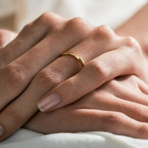 mão feminina com aliança de casamento feita à mão em ouro 18k que o par forma um coração minimalista
