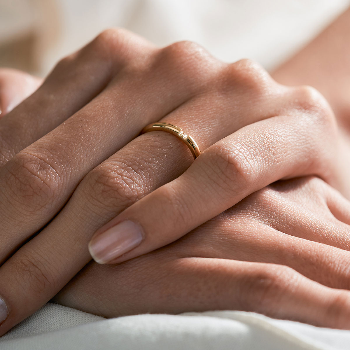 mão feminina com aliança de casamento feita à mão em ouro 18k que o par forma um coração minimalista