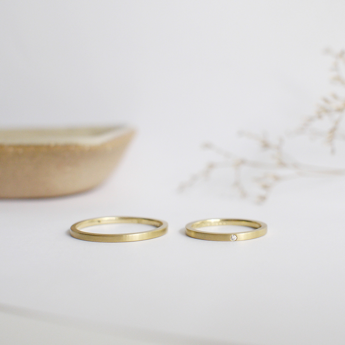 par de alianças finas de casamento feitas a mão em ouro 18k e diamante central minimalistas sobre fundo branco