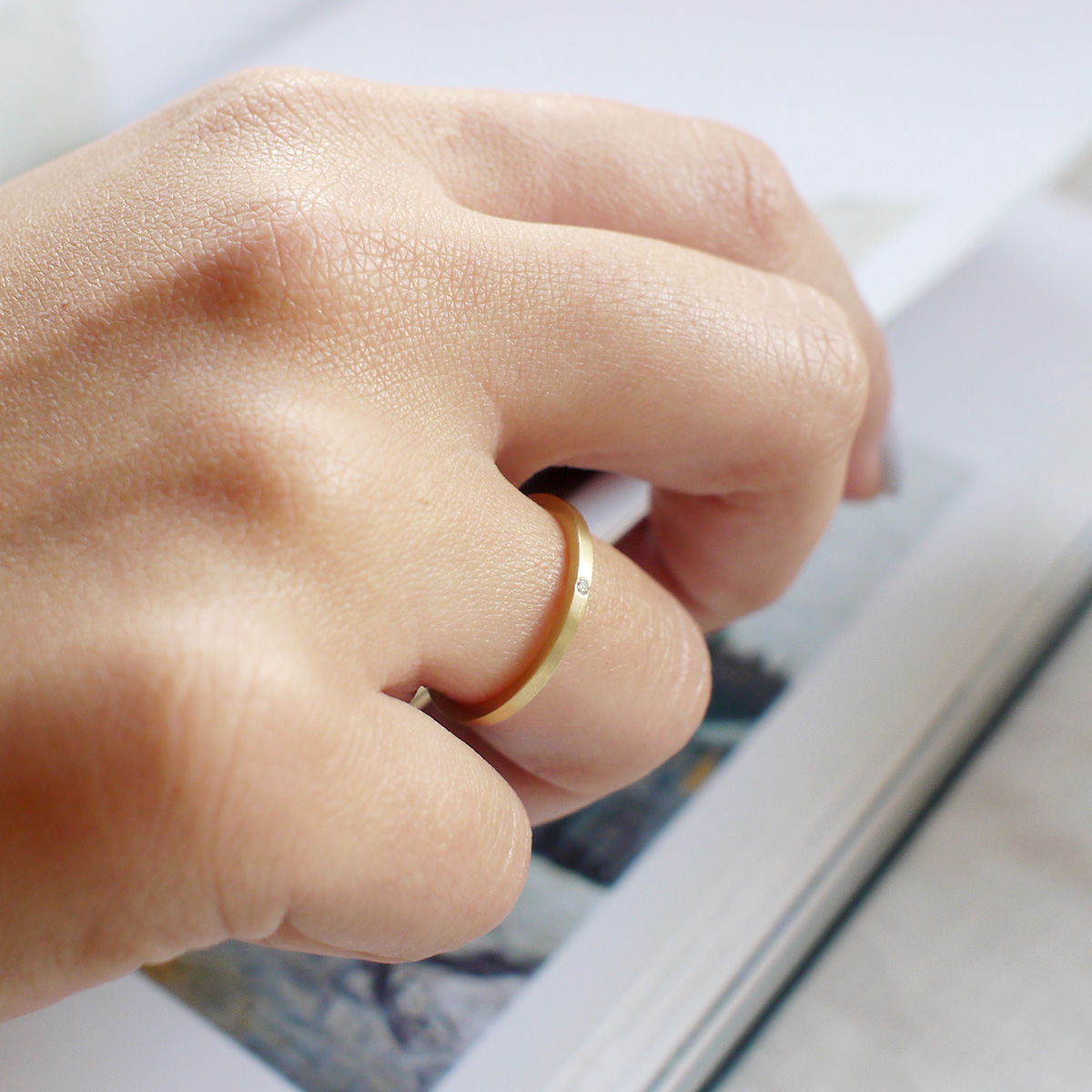 mão feminina com aliança fina de casamento feita a mão em ouro 18k e diamante central minimalista