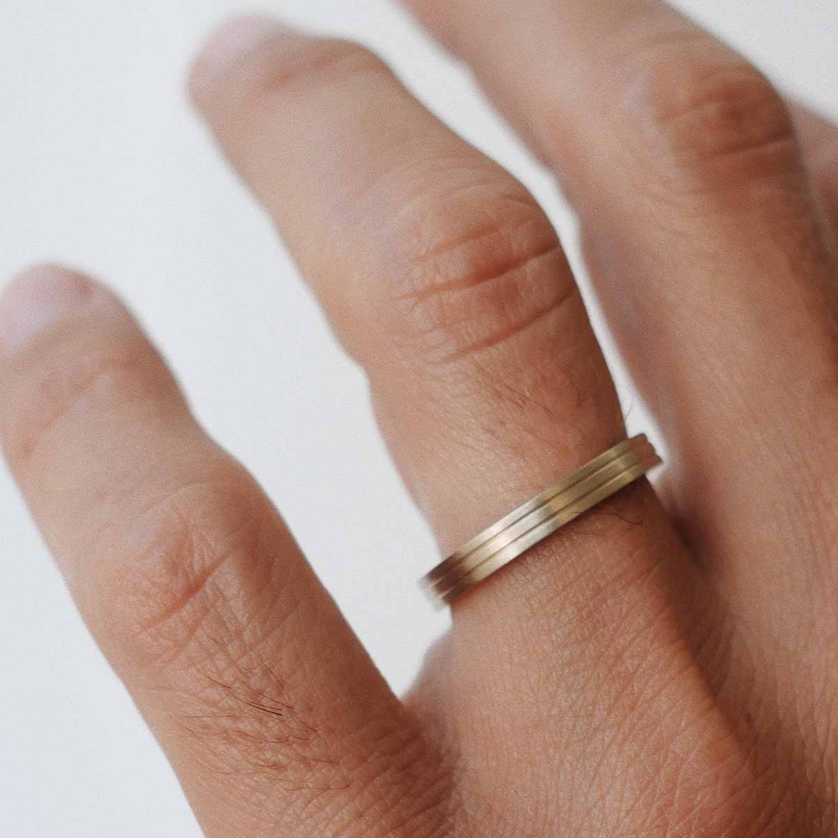 Mão masculina usando aliança de casamento feita a mão em ouro 18k com detalhes de linhas minimalista
