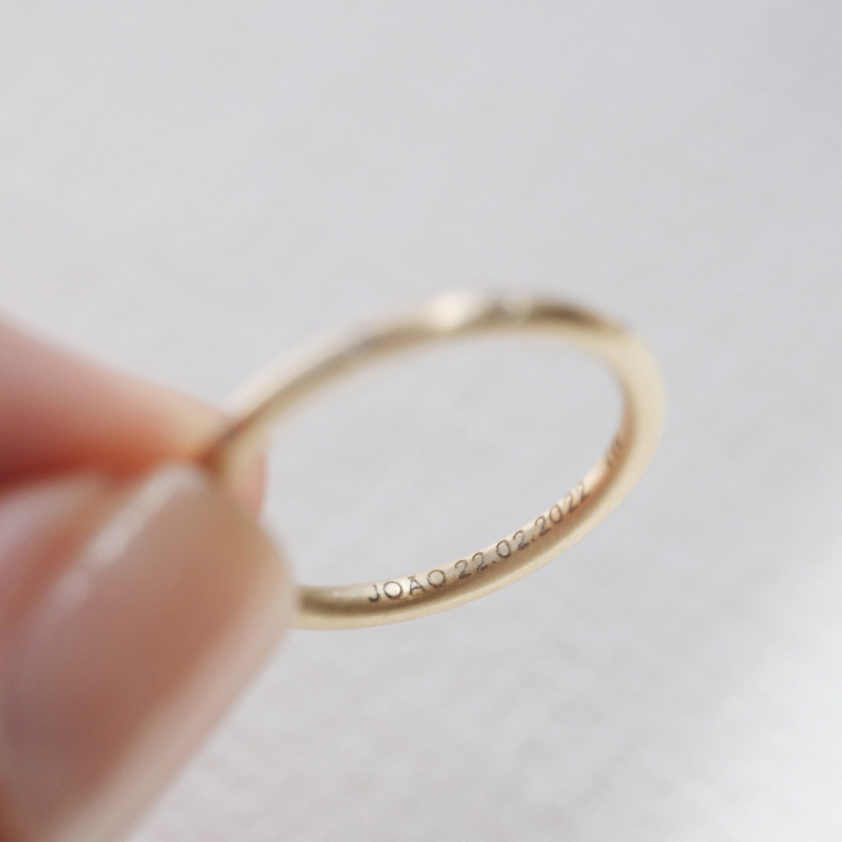 Mão feminina segurando Aliança de aro redondo 1,8mm minimalista feita a mão em ouro 18k para casamentos sobre tecido branco