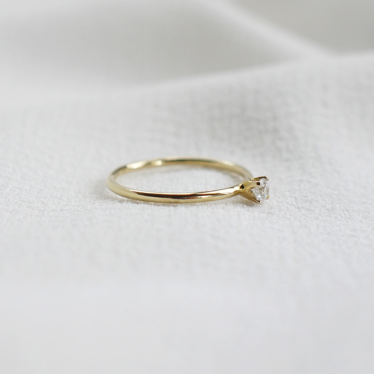 Anel de noivado minimalista feito a mão em ouro 18k com diamante sobre tecido branco