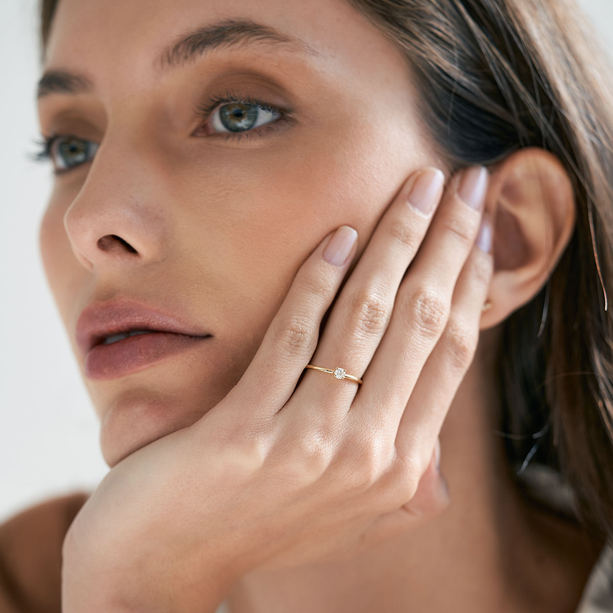 Mulher com o rosto apoiado n maõ usando anel de noivado minimalista feito a mão em ouro 18k com diamante