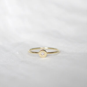 Anel de aro fino minimalista feito a mão em ouro 18k com diamante no centro sobre tecido branco