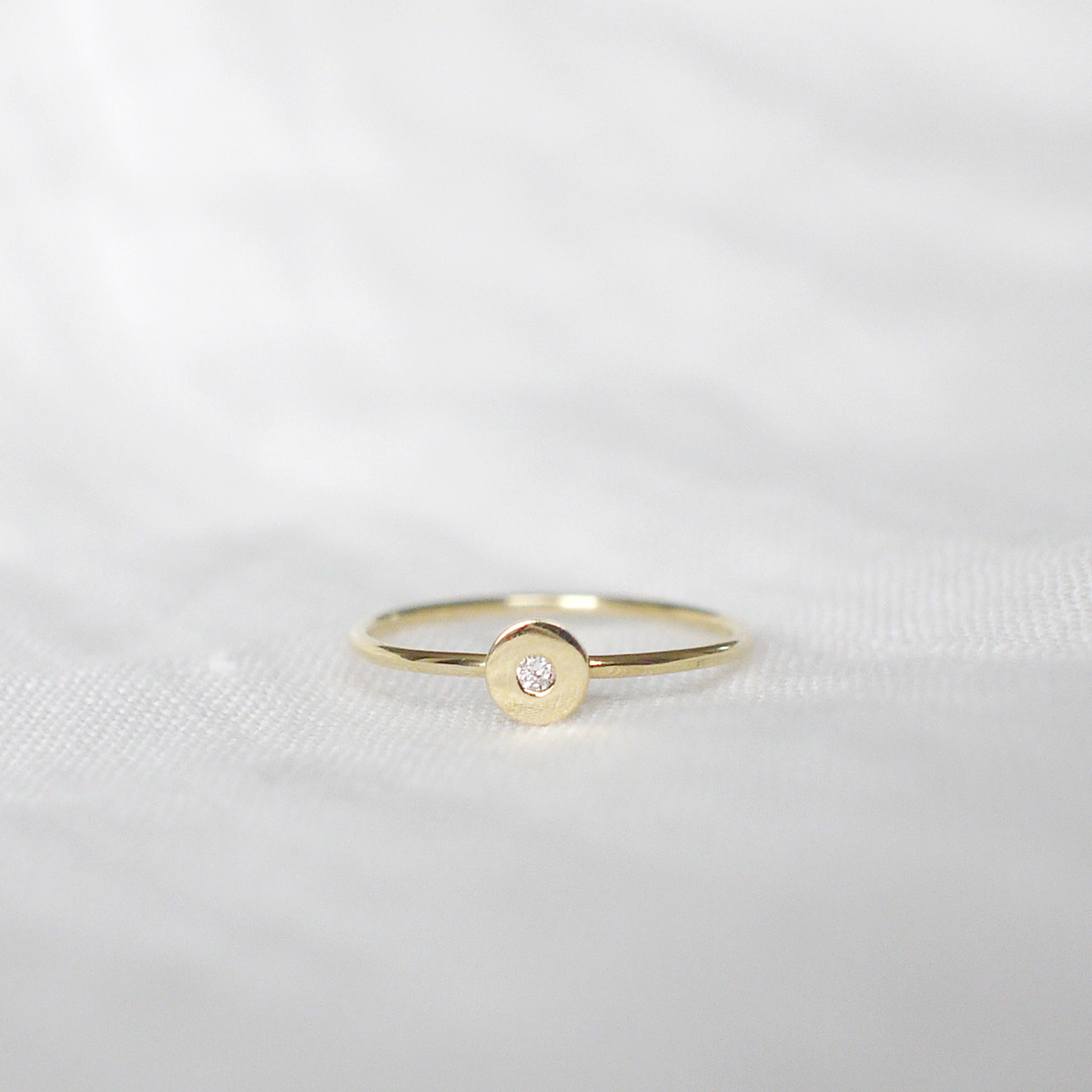 Anel de aro fino minimalista feito a mão em ouro 18k com diamante no centro sobre tecido branco