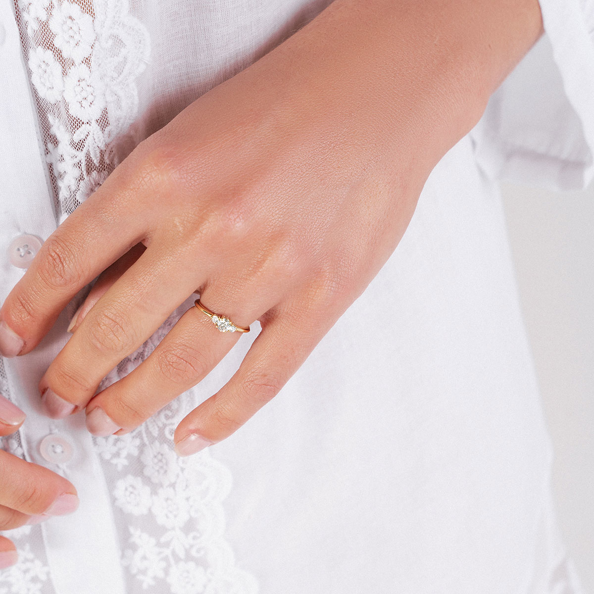 Mulher de blusa de renda branca usando Anel de noivado minimalista e feito a mão em ouro 18k com três diamantes