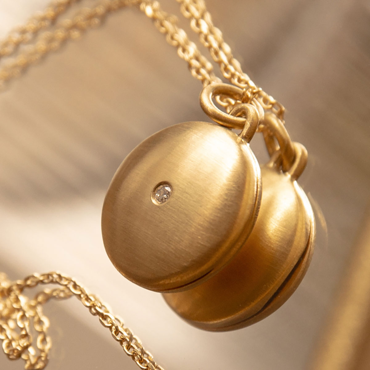 pingente relicário de formato redondo feito à mão em ouro 18k com espaço para duas fotos no interior e um diamante pequeno na parte de fora central