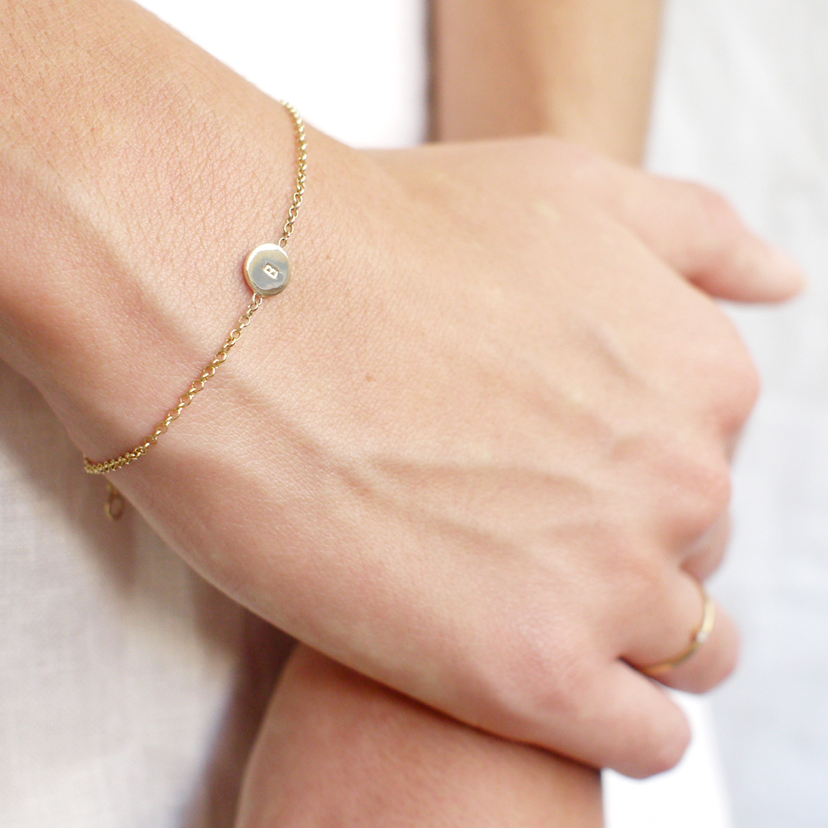 Mulher usando Pulseira feita a mão em ouro 18k com plaquinha gravada com letra