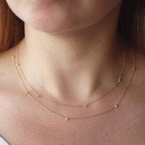 Mulher usando dois colares delicados e minimalistas feitos a mão em ouro 18k com pequenos diamantes