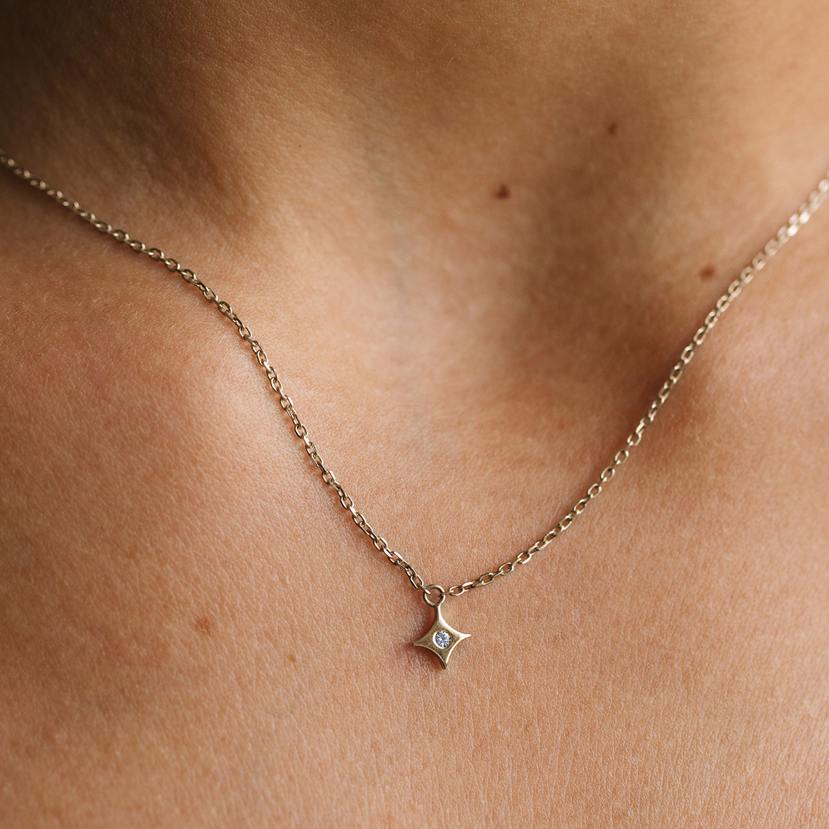 Mulher usando colar feito a mão em ouro 18k com pingente de estrela com diamante no centro minimalista