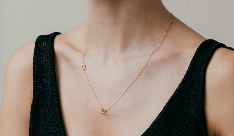 mulher de pele clara e blusa preta usando colar minimalista feito à mão em ouro 18k com fecho T modelo gravatinha de duas regulagens
