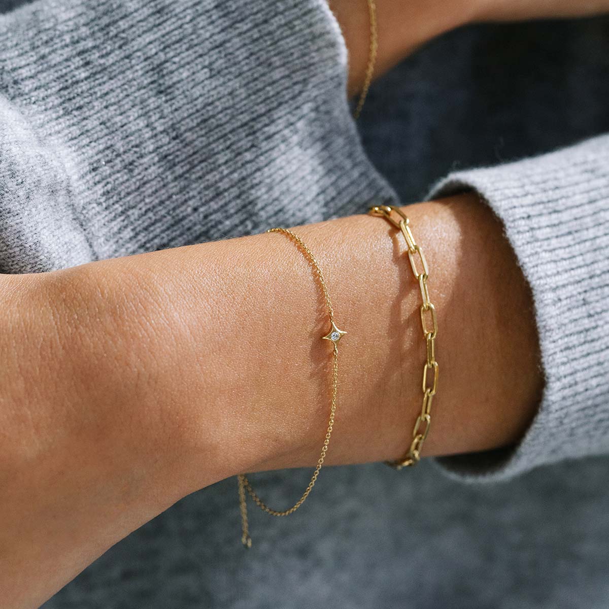 Mão feminina usando pulseiras feitas à mão em ouro 18k com pingente em formato de estrela com diamante no centro