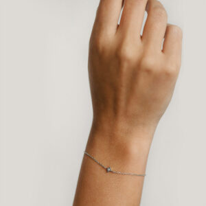 Mão feminina usando pulseira feita à mão em ouro branco 18k com pingente em formato de estrela com diamante no centro