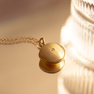 pingente relicário de formato redondo feito à mão em ouro 18k com espaço para duas fotos no interior e um diamante pequeno na parte de fora central