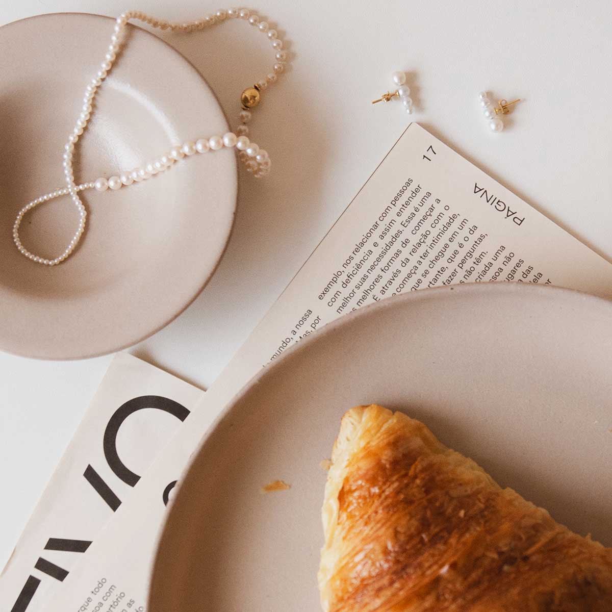 fotografia flatlay joias de pérolas, croissant e café