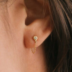 Mulher usando Brinco minimalista feito a mão em ouro 18k com diamante na ponta e corrente ligando a tarraxa