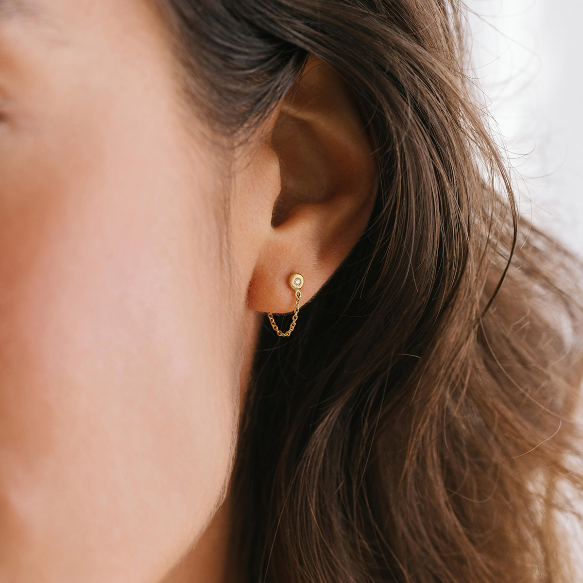Mulher usando Brinco minimalista feito a mão em ouro 18k com diamante na ponta e corrente ligando a tarraxa