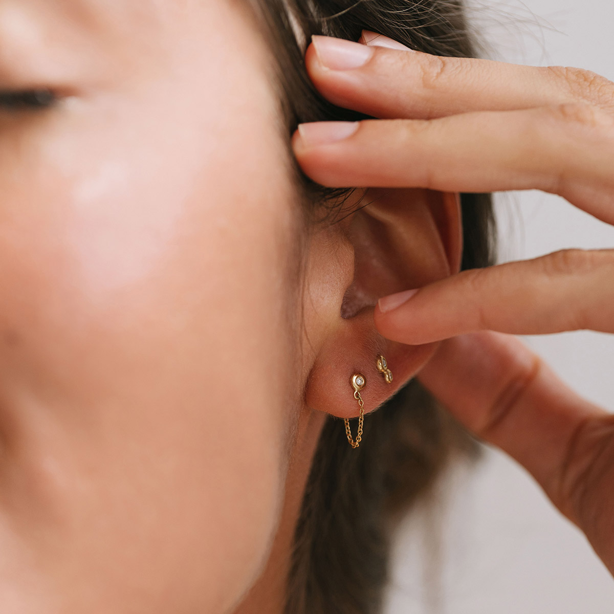 Mulher usando Brincos minimalistas feitos a mão em ouro 18k com diamantes e corrente ligando a tarraxa
