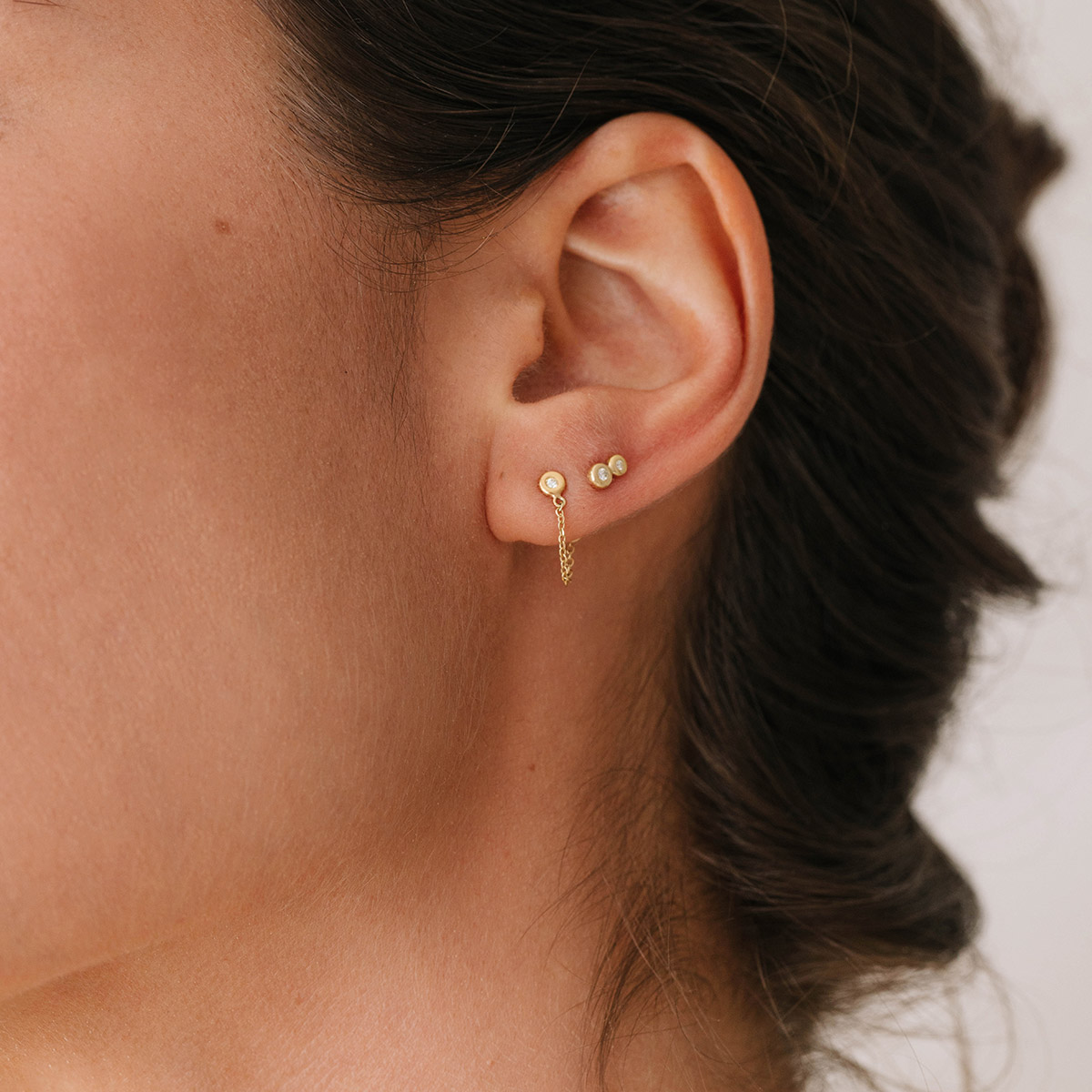 Mulher usando Brincos minimalistas feitos a mão em ouro 18k com diamantes e corrente ligando a tarraxa