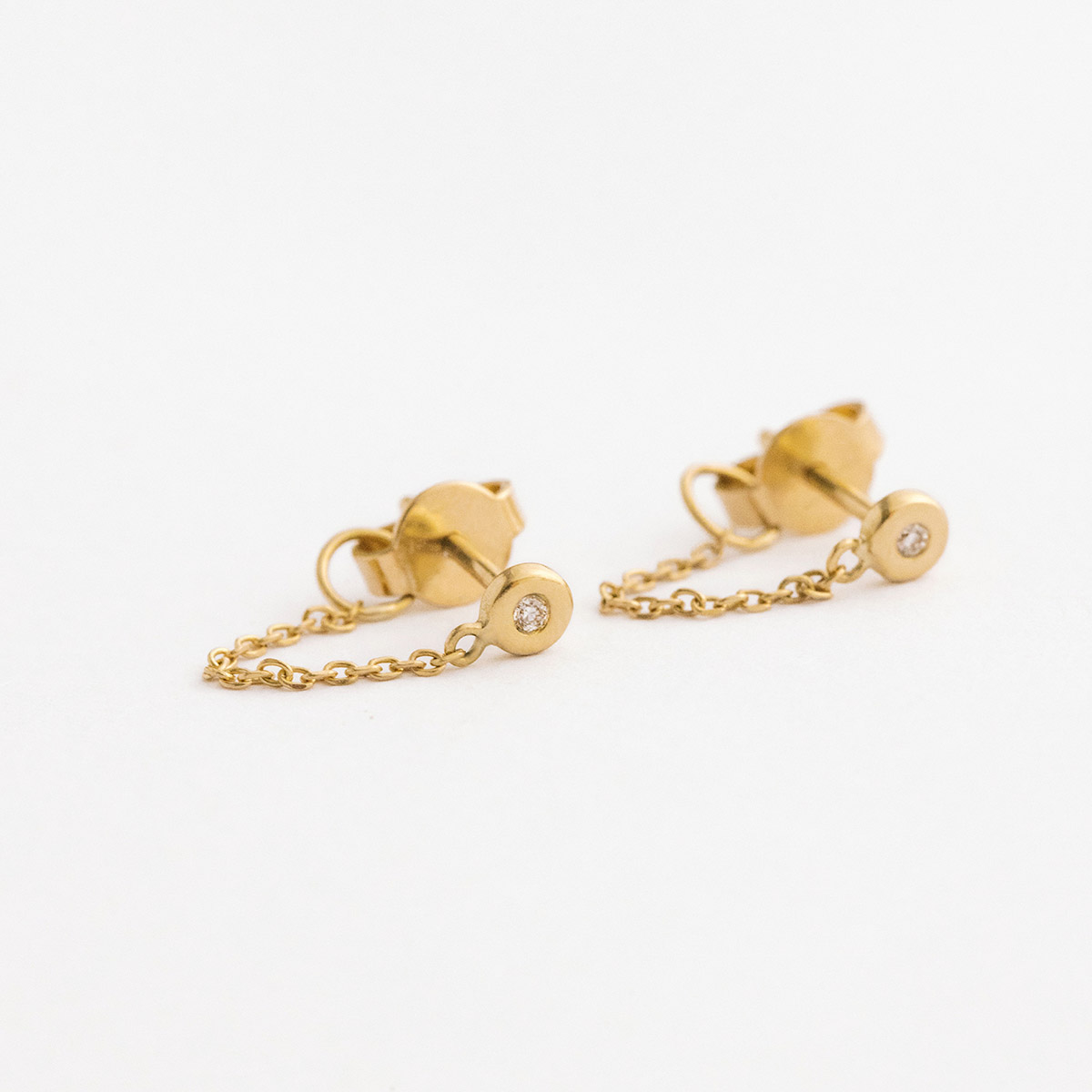 Brinco minimalista feito a mão em ouro 18k com diamante na ponta e corrente ligando a tarraxa