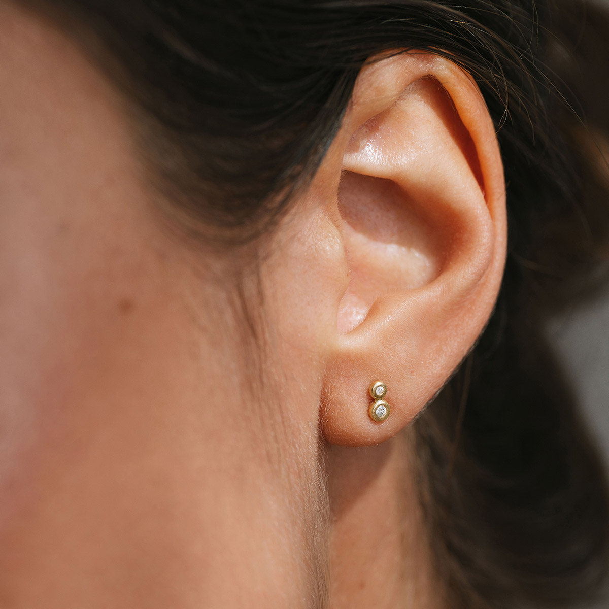 Mulher usando Brinco delicado minimalista feito a mão em ouro 18k com dois diamantes de diferentes tamanhos