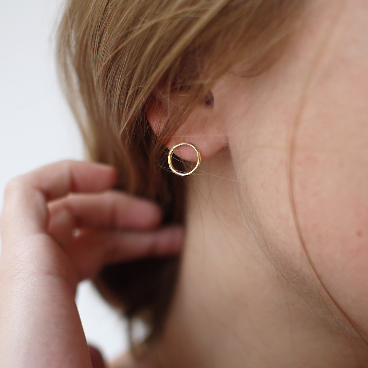 Mulher usando Brinco minimalista em forma de círculo vazado feito a mão em ouro 18k com textura martelada