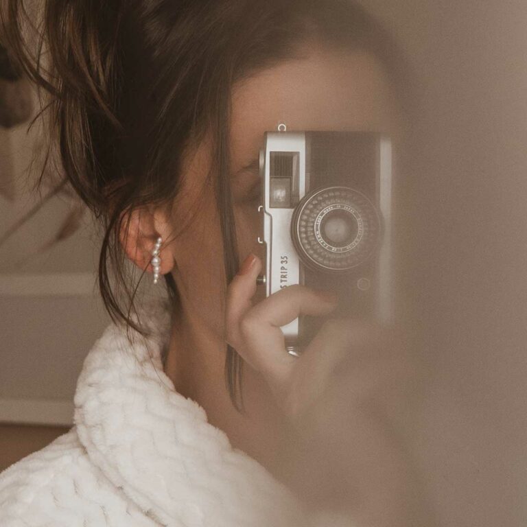 Mulher tirando foto com câmera usando Brinco minimalista feito a mão em ouro 18k com sete pérolas naturais em tamanhos diferentes