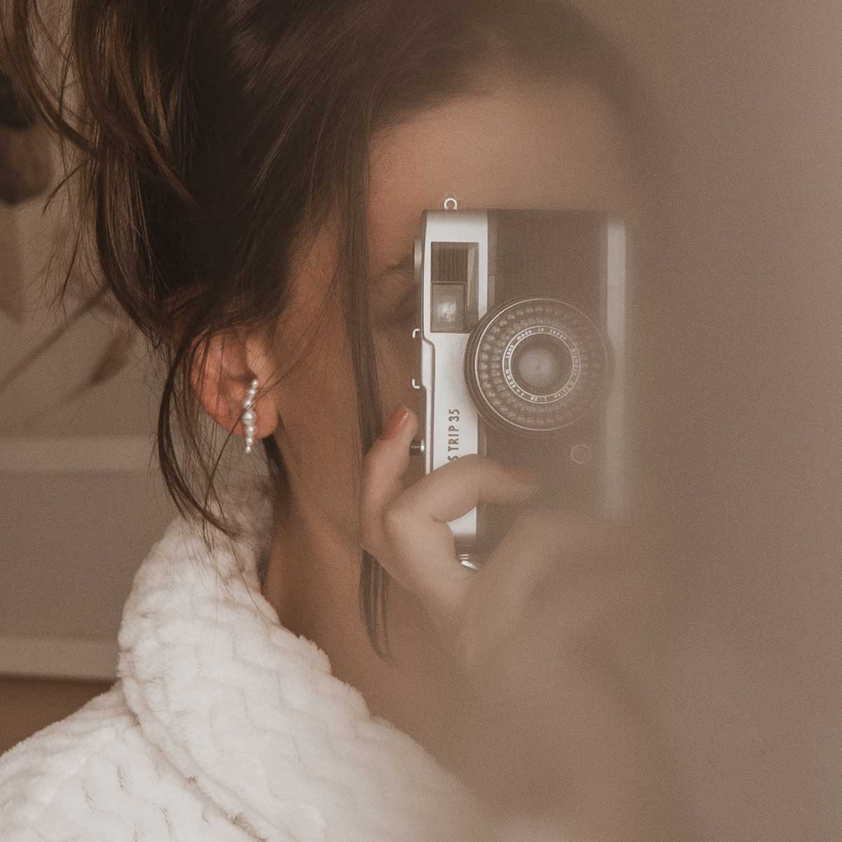 Mulher tirando foto com câmera usando Brinco minimalista feito a mão em ouro 18k com sete pérolas naturais em tamanhos diferentes