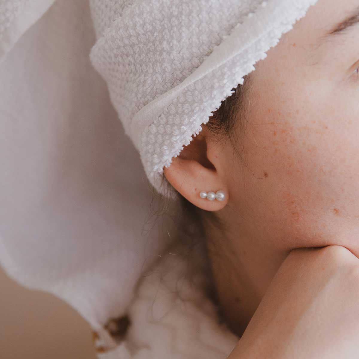 Mulher de toalha usando Brinco minimalista feito a mão em ouro 18k com três pérolas naturais em tamanhos diferentes