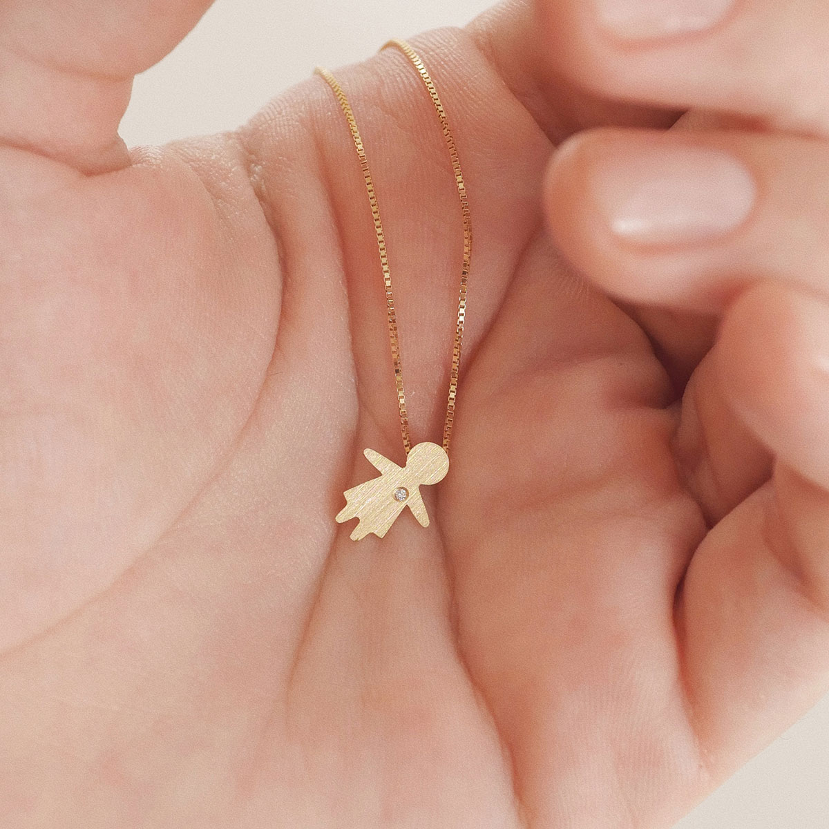 Colar com pingente bambina em ouro 18k com diamante apoiado na mão, representando filha e amor materno