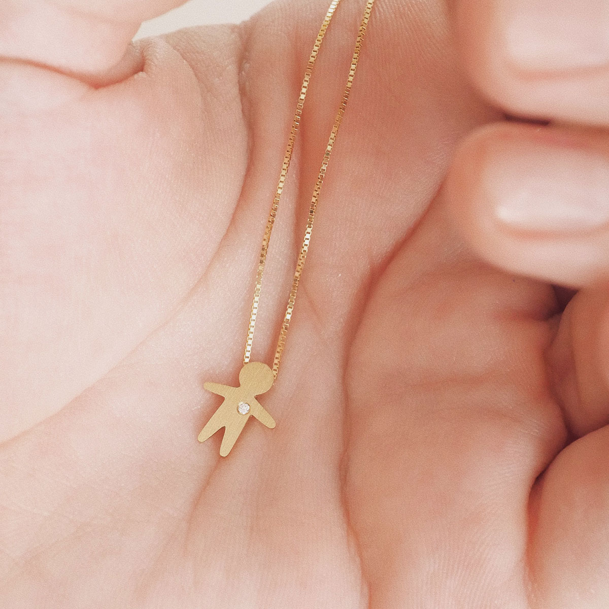 Colar com pingente bambino em ouro 18k com diamante apoiado na mão, simbolizando filho e afeto