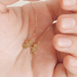 Colar com pingentes bambinos duplos em ouro 18k com diamantes apoiado na mão, simbolizando amor entre filhos