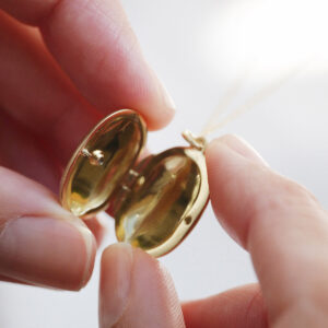 Mulher segurando pingente relicário em formato oval minimalista feito a mão em ouro 18k com diamante no lado de fora e dois espaços para foto
