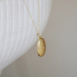 Mulher usando pingente relicário em formato oval minimalista feito a mão em ouro 18k com diamante no lado de fora e dois espaços para foto