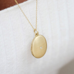 Mulher usando pingente relicário em formato oval minimalista feito a mão em ouro 18k com diamante no lado de fora e dois espaços para foto