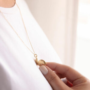 Mulher usando Corrente com pingente relicário em formato redondo minimalista feito a mão em ouro 18k com diamante no lado de fora e dois espaços para foto