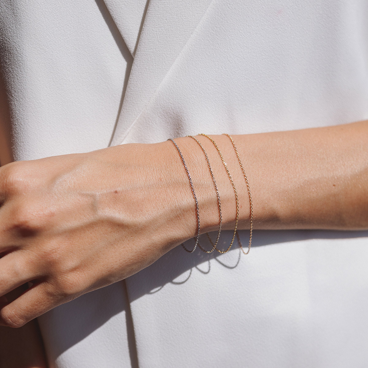 Mulher usando pulseiras minimalistas de diferentes tonalidades feitas a mão em ouro 18k
