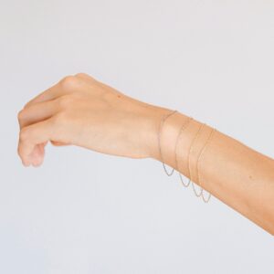 Mulher usando pulseiras minimalistas de diferentes tonalidades feitas a mão em ouro 18k