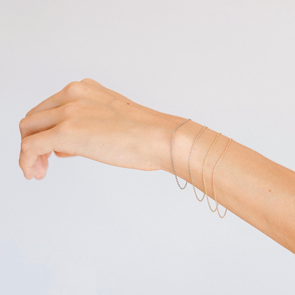 Mulher usando pulseiras minimalistas de diferentes tonalidades feitas a mão em ouro 18k