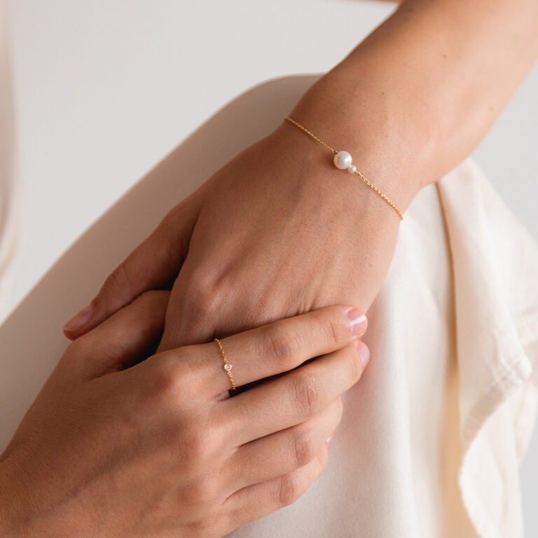 Mulher usando joias minimalistas, pulseira e anel feito à mão em ouro 18k com pérolas e pedras naturais